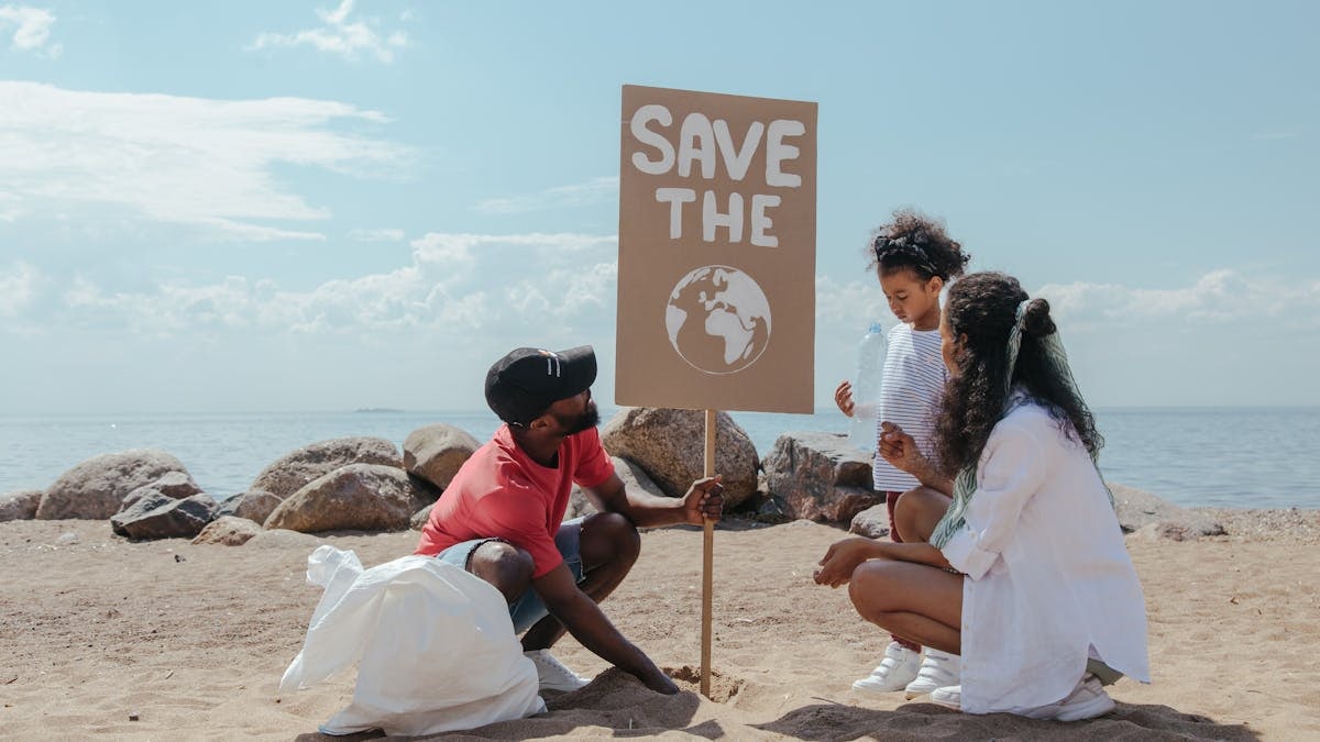 Family cleans beach, promoting environmental awareness with 'Save the Planet' sign.