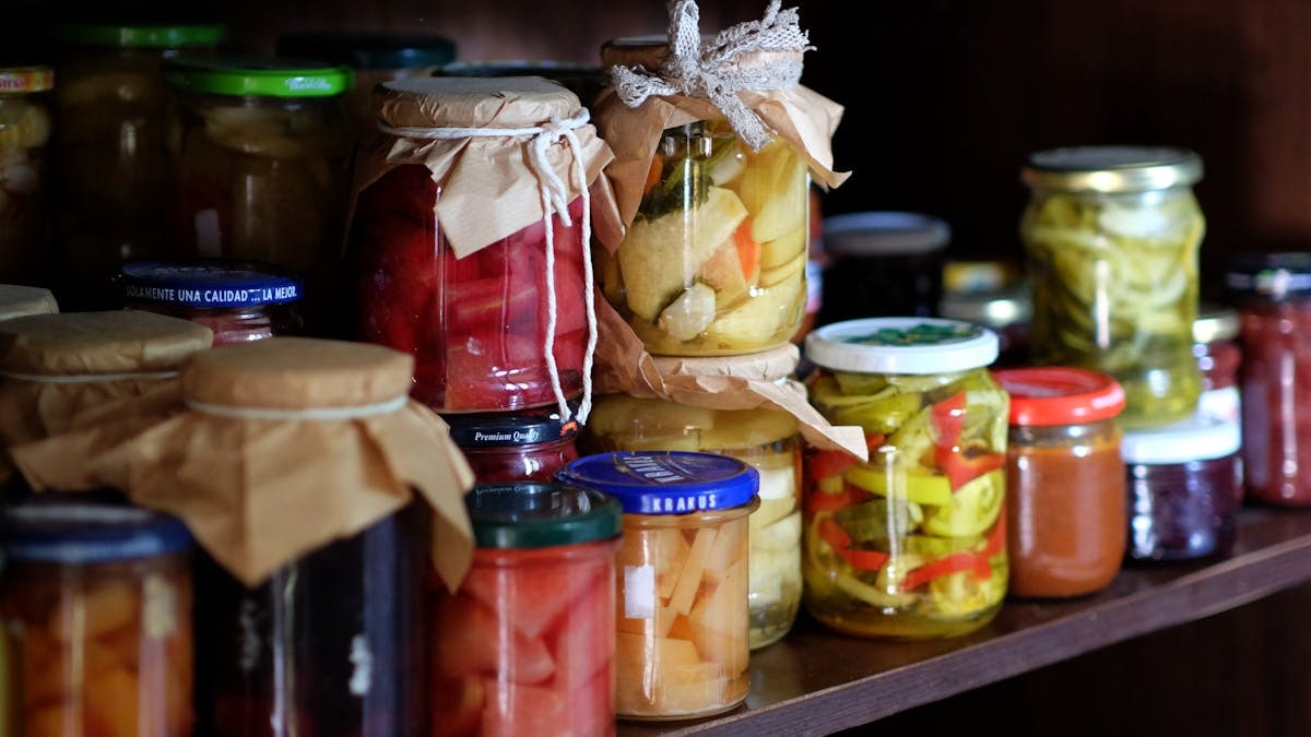 A variety of homemade preserves and pickles stored on a rustic wooden pantry shelf.